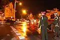 A speeding motorcade of cars. The military leaders on their way from the royal palace as the military police look on.