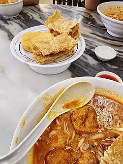 Image 25A bowl of curry mee, with fried beancurd skins and fish cake on the side (from Malaysian cuisine)