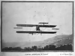 A biplane in flight. A man is visible at the controls.
