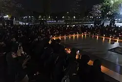 Photo showing a crowd dressed in all black congregating around a candlelight vigil held in Airlangga University