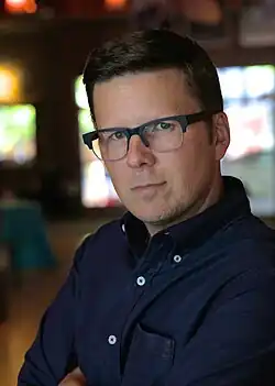 Photo of Rodríguez, a clean-shaven Cuban-American man, with short dark hair, glasses with dark frames, and a dark button-up shirt.