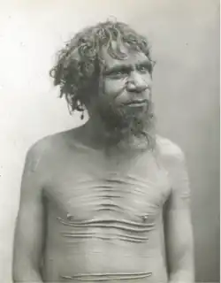 Portrait photograph of a shirtless Aboriginal man with a scarred torso.
