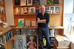 Man with gray hair standing with arms crossed in bookstore