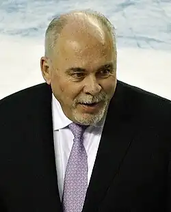 Middle-aged man with grey hair, wearing a navy blue suit jacket