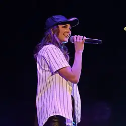 A woman wearing a cap and smiling while holding a microphone in her hand