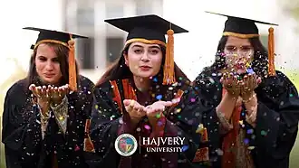 Female graduates wearing academic regalia celebrate during a graduation ceremony.