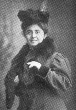 A white woman, smiling, wearing a hat, a coat, and a fur stoll.