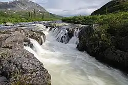 A river runs through a small rocky waterfall in a mountain range