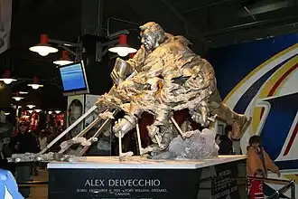 A large bronze statue of an ice hockey player in the act of shooting the puck. The player's hands and stick are shown numerous times to simulate motion. At the base of the statue is inscribed "Alex Delvecchio Born: December 4, 1931, Fort William, Ontario, Canada
