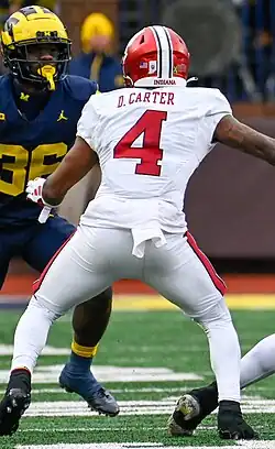 American wide receiver Dequece Carter playing for the Indiana Hoosiers against Michigan in 2023. He is wearing a white jersey with the picture showing the back of it, with his name, Carter, and number, 4, in red. He is also wearing a red helmet with a white stripe down the middle.