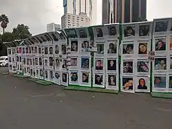 Long outdoor display of printed portraits arranged in rows along a street, each showing a different missing person with names and details beneath the photos.