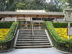 A flight of stairs leads to an old-fashioned railroad station platform with an old-fashioned railroad depot building in the background.