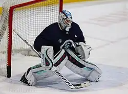 Ice hockey goaltender in a Seattle Kraken jersey holding his stick out and anticipating the puck