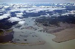Aerial photo of the mouth of a river with several small islands, next to a sandy peninsula with mountains in the background