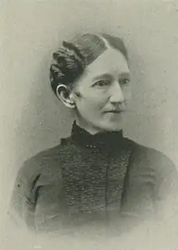 19th-century B&W portrait photo of a woman with her hair in an up-do, wearing a dark, fitted blouse.