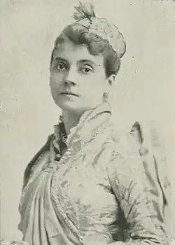 B&W portrait photo of a middle-aged woman wearing a pale, high-collared blouse and a hat, with her hair in an up-do.