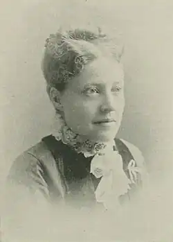 19th-century B&W portrait photo of a woman with her hair in an up-do, wearing a dark, fitted blouse.