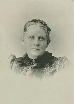 19th-century B&W portrait photo of a woman with her hair in an up-do, wearing a dark, fitted blouse.