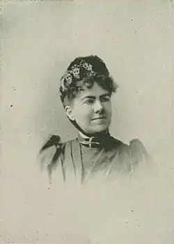 19th-century B&W portrait photo of a woman with her hair in an up-do, wearing a dark, fitted blouse.