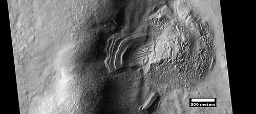 Layered feature that is probably the remains of a once widespread unit that fell from the sky, as seen by HiRISE under the HiWish program. Dipping layers are common in some regions of Mars. They may be the remains of mantle layers. Another idea for their origin was presented at 55th LPSC (2024) by an international team of researchers. They suggest that the layers are from past ice sheets.[66]