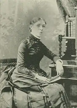 19th-century B&W portrait photo of a woman with her hair in an up-do, wearing a dark, fitted blouse.