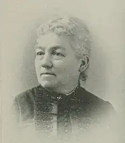 19th-century B&W portrait photo of an elderly woman with her hair in an up-do, wearing a dark, fitted blouse.