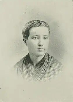 19th-century B&W portrait photo of a woman with her hair in an up-do, wearing a dark, fitted blouse.