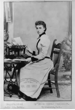 B&W portrait photo of a young seated woman wearing a pale, high-collared blouse with her hair in an up-do.