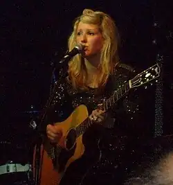 Goulding holding a guitar and singing