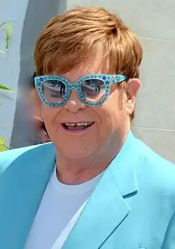 Elton John wearing a blue suit with matching bedazzled glasses