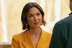 close-up of Emily Chang wearing a yellow jacket, looking left and up at barely visible interlocutor, with slight squint