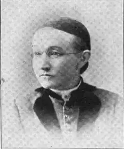 19th-century B&W portrait photo of a woman with her hair in an up-do, wearing a dark, fitted blouse.