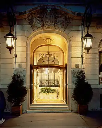 Ornate hotel entrance with arched glass doors, decorative stonework, and flanking lanterns