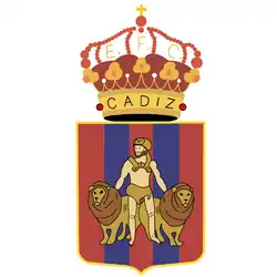 A coat of arms showing a male hero in a loincloth and fur hat holding two male lions. The field is five vertical stripes: three red and two blue. A crown surmounts the coat of arms: the ring of the crown reads "CADIZ". Among the beams of the crown, the letters "E F C".