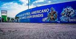 Exterior wall of Estadio Samuel León Brindis painted blue, displaying the stadium name and a mural with American football imagery.