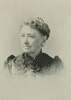 19th-century B&W portrait photo of a woman with her hair in an up-do, wearing a dark, fitted blouse.