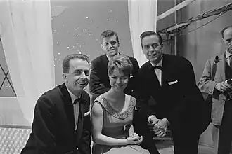 Black-and-white photograph; Carroll, Kok and Rekkers dressed in tuxedos, Froboes in a V-neck dress with the collar adorned with jewels