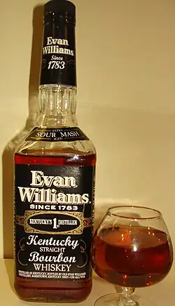 A color photograph of a bottle of bourbon to the left of a glass containing some of that bourbon