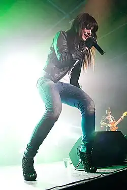 Ewa Farna singing on stage wearing low-rise jeans, a black leather jacket, and a white shirt.