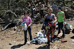 Teenagers picking up belongings from a pile of rubble and scattered trees