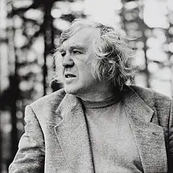 middle-aged man with medium-length gray, wearing a jacket, trees in the background, half profile