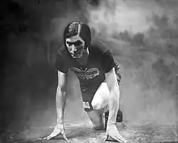 Black-and-white studio portrait of Bobbie Rosenfeld in athletic clothing, posed in a crouched stance with one knee forward and both hands on the ground against a plain backdrop.