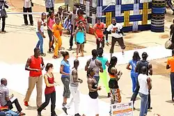 An image from a high angle of a group of Burkinabe in colorful clothing standing around a white catwalk on the ground.