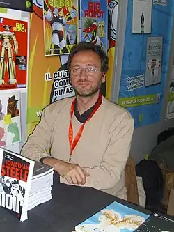 Federico Memola wearing a cream top sitting in a comics shop against a wall covered in posters