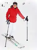 A female skier in winter clothes: jacket, hat, thick gloves, warm pants and ski boots