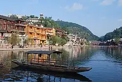 photograph of a sunny riverbank full of buildings with a boat on the river in the foreground