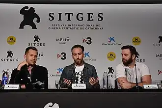 An image of Aaron Moorhead, Justin Benson, and David Lawson sitting at a table at the Sitges Film Festival in 2019. The trio are the founders of the Rustic Films production company and co-produce many films together.