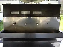 Metal drinking fountain with three taps and information signs over each of them