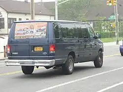 Navy blue 2003-2007 Ford Econoline full-sized 15 passenger van featuring the body extension added to allow for the installation of an additional row of seating completely behind the rear axle. The vans have a small additional window behind the rearmost side window signifying the extended length over a regular 12 passenger van.