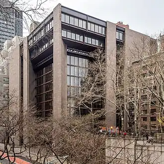 The southern and eastern facades of the Ford Foundation Building as seen from the southeast. The outer ends of each facade are made of pink granite. In between are glass walls within steel frames, which are mostly recessed from the facade, except at the top of the building.